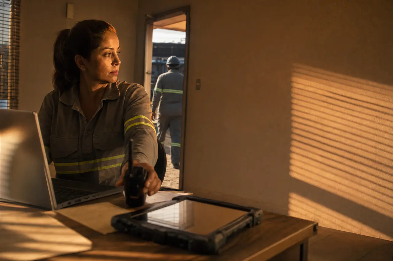 Coordenadora de turno alcançando o rádio na mesa da sala de operação ao amanhecer